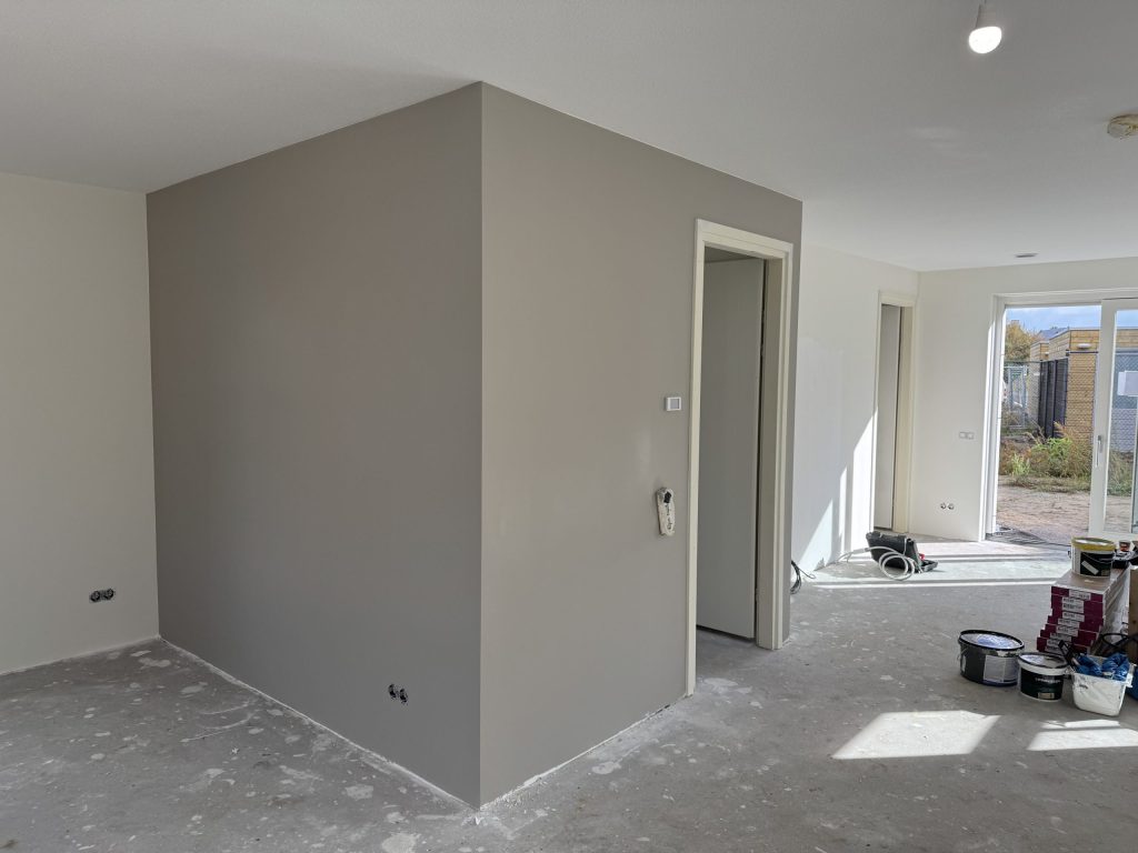 Nieuwbouwwoonkamer met een pas gesausde grijze wand en verfemmers op de betonvloer