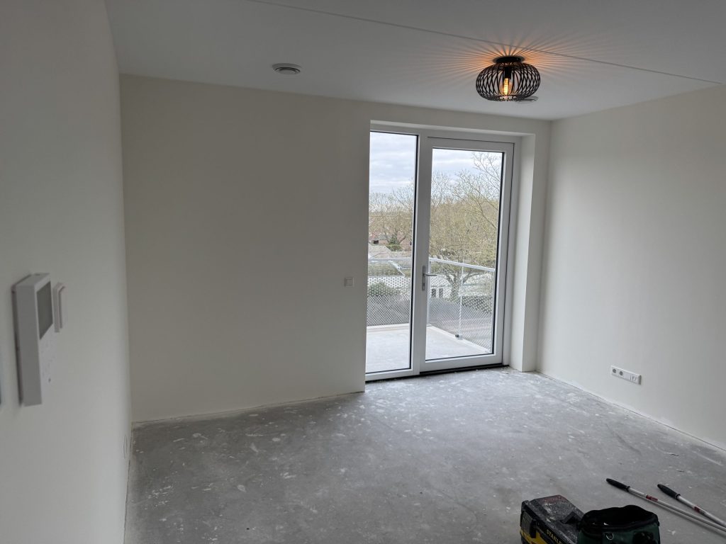 Nieuw appartement met witte wanden, een betonvloer en openslaande deuren naar het balkon